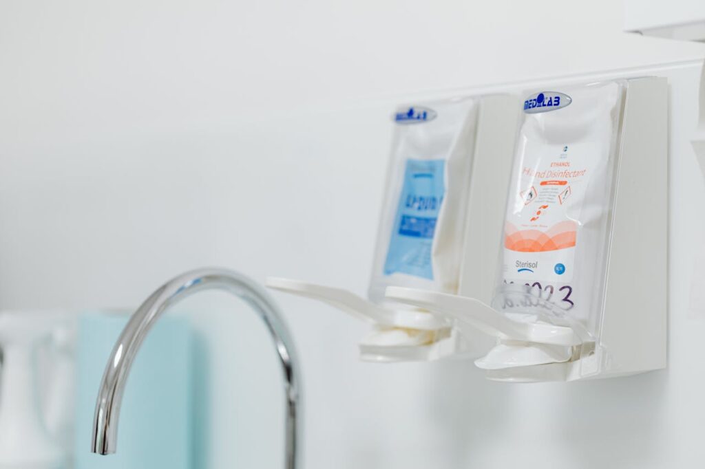 pexels-photo-6627791 Close-up of wall-mounted dispensers for hand sanitizers next to a hygienic sink faucet.