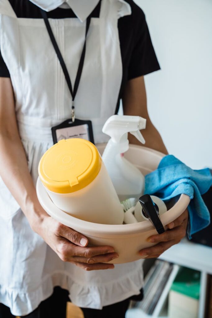 pexels-photo-9462663 A uniformed cleaner holding a basin with cleaning supplies indoors. Ideal for cleaning and sanitation themes.